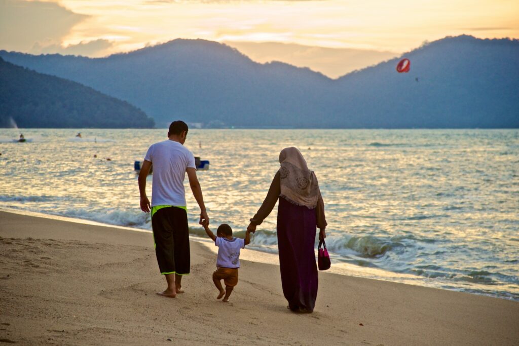 What makes a good foster carer man and woman holding toddler's hands while walking on beach with the sun setting in the background
