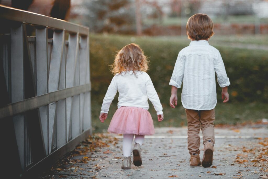 fostering siblings manchester two little children walking next to each other by a wooden fence